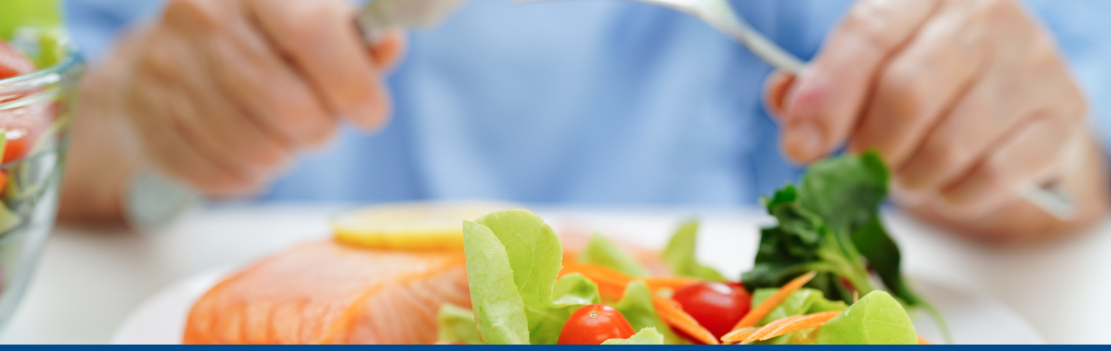 A person eating from a plate of healthy foods including salad and salmon